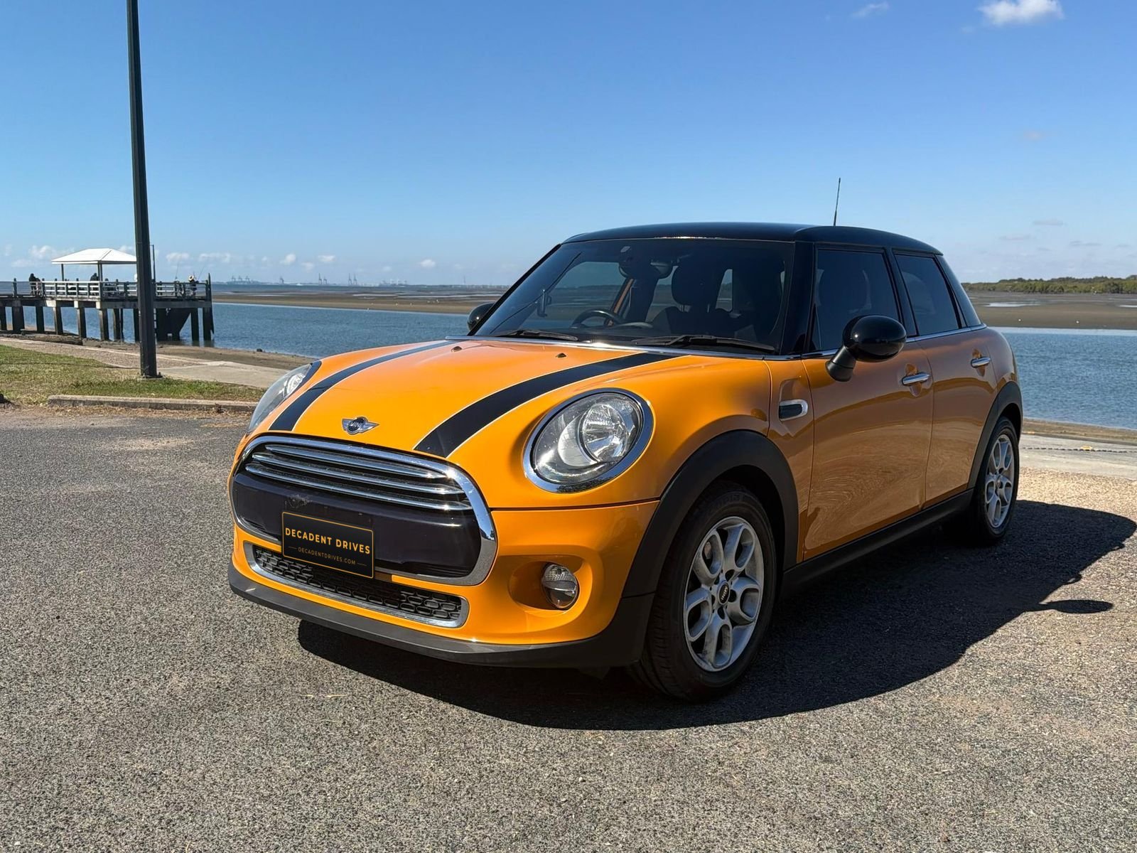 Orange 2015 MINI Cooper 5-door hatch, front three-quarter view by the water – Decadent Drives hire car, Brisbane