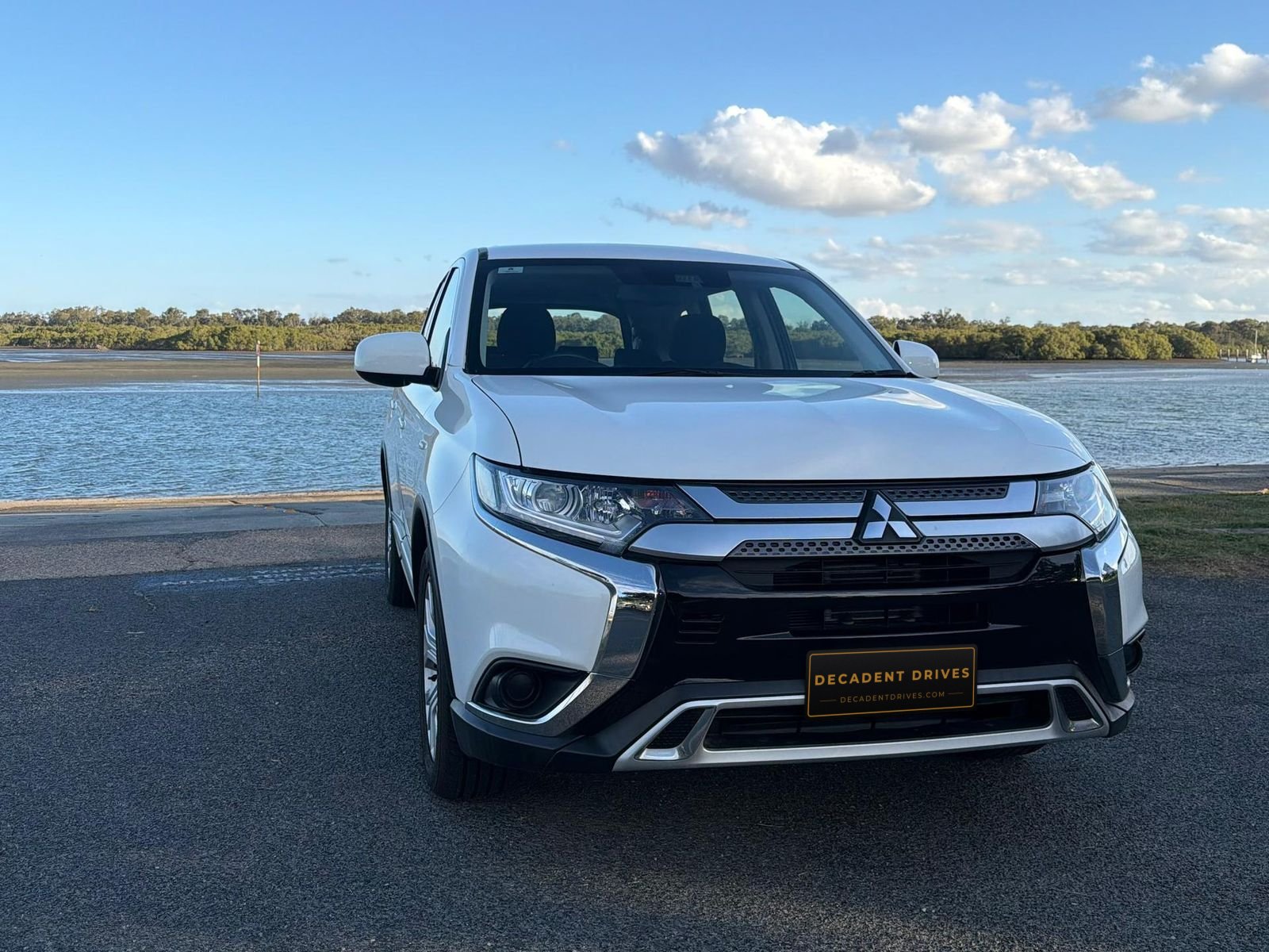 White 2020 Mitsubishi Outlander 7-seat SUV, front view by the water – Decadent Drives hire car, Brisbane
