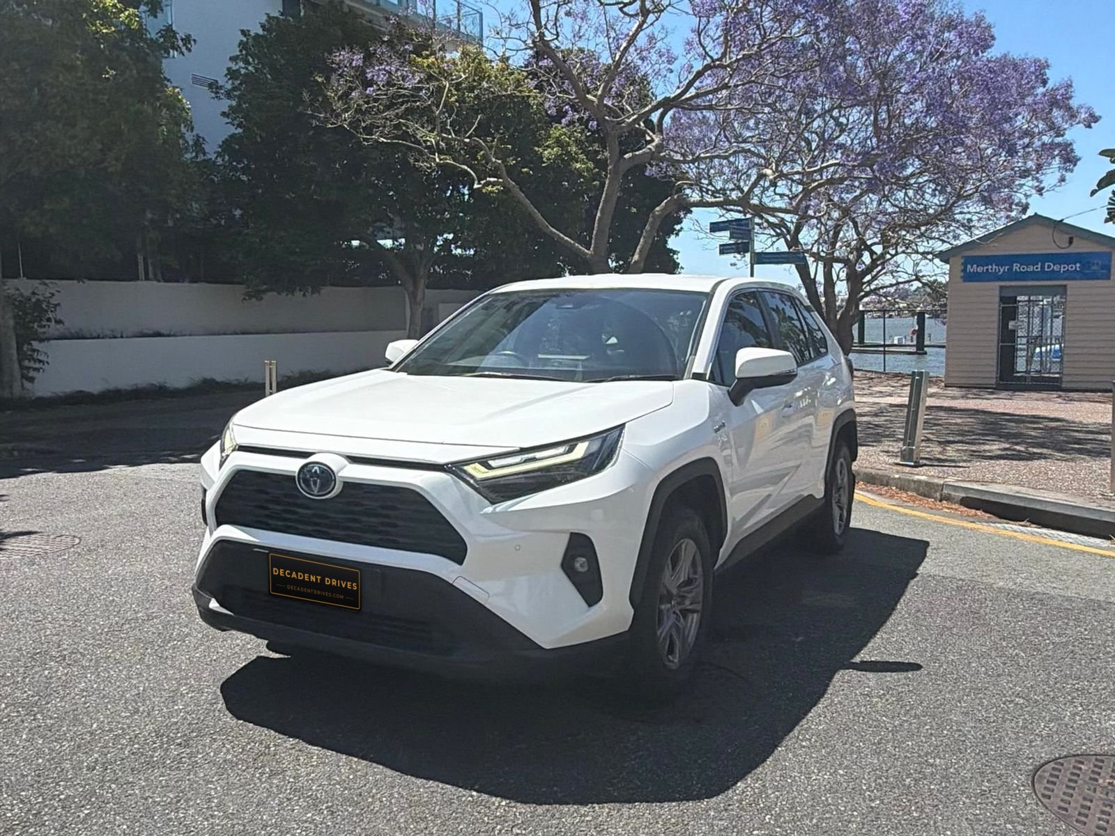 White 2023 Toyota RAV4 Hybrid SUV, front three-quarter view under jacaranda trees